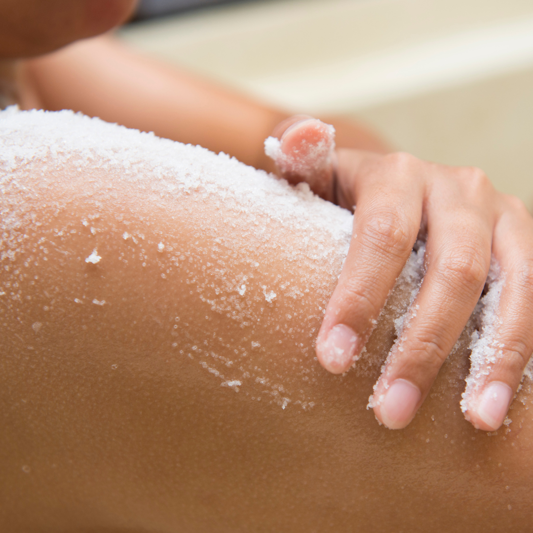 Woman using a botanical sugar scrub on her arm to gently exfoliate and reveal softer, smoother skin.